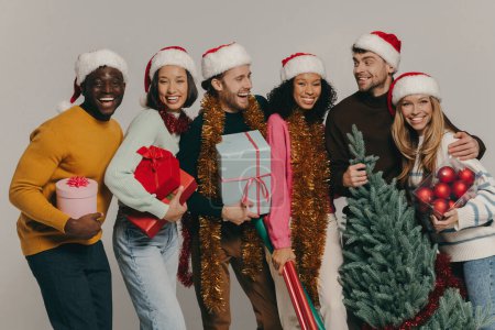Téléchargez les photos : Heureux les jeunes portant l'arbre de Noël et divers ornements sur fond de studio - en image libre de droit