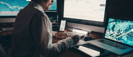 Téléchargez les photos : Gros plan trader masculin analysant les données boursières tout en étant assis au poste de travail de bureau avec plusieurs ordinateurs - en image libre de droit