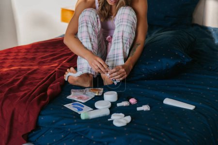 Téléchargez les photos : Gros plan de la jeune femme peignant des ongles de pieds tout en faisant pédicure sur le lit à la maison - en image libre de droit