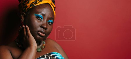 Foto de Primer plano de hermosa mujer africana de talla grande con hermoso maquillaje con atuendo tradicional sobre fondo rojo - Imagen libre de derechos