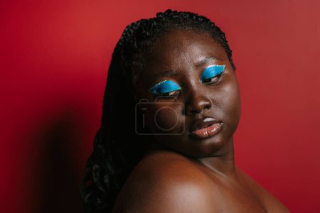 Téléchargez les photos : Superbe femme africaine taille plus avec beau maquillage debout sur fond rouge - en image libre de droit