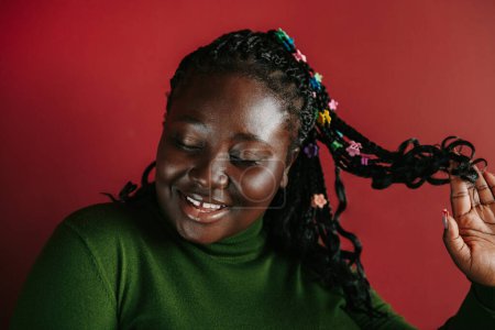 Téléchargez les photos : Belle femme africaine avec des cheveux tressés et des clips colorés souriant sur fond rouge - en image libre de droit