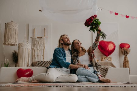 Téléchargez les photos : Joyeux jeune couple amoureux célébrant la Saint-Valentin à la maison avec des ballons coeur rouge sur fond - en image libre de droit