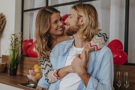 Téléchargez les photos : Jeune couple aimant embrasser et sourire tout en célébrant la Saint-Valentin à la maison décorée - en image libre de droit