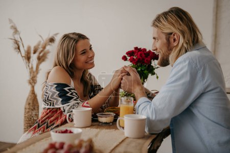 Photo for Young loving couple holding hands while enjoying healthy breakfast at boho style home - Royalty Free Image