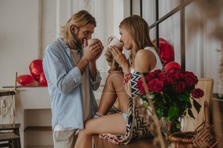 Téléchargez les photos : Jeune couple romantique boire du café à partir de tasses tout en passant du temps à la maison ensemble - en image libre de droit