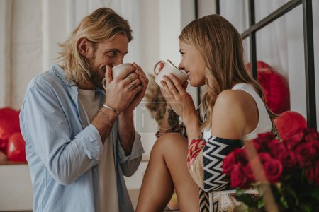 Foto de Joven pareja amorosa disfrutando del café de la mañana de tazas mientras pasan tiempo en la casa decorada juntos - Imagen libre de derechos
