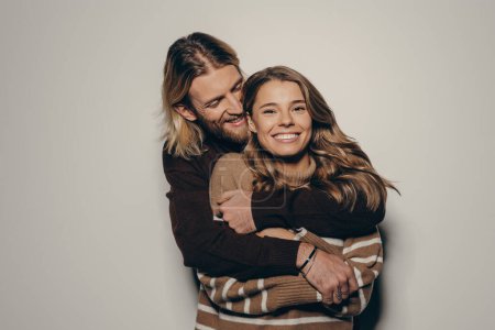 Téléchargez les photos : Heureux jeune couple aimant dans des vêtements chauds accueillants tout en se tenant debout sur fond beige - en image libre de droit