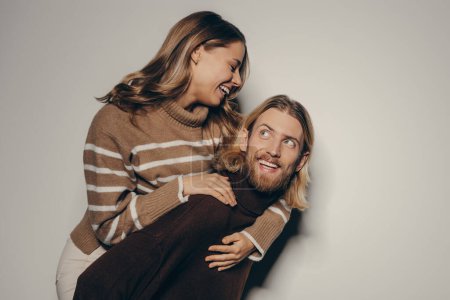 Téléchargez les photos : Heureux jeune homme élégant piggyback sa belle petite amie tout en se tenant sur fond beige - en image libre de droit