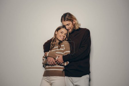 Photo for Fashionable young loving couple in cozy warm wear embracing while standing on beige background - Royalty Free Image