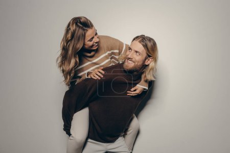 Téléchargez les photos : Joyeux jeune homme élégant tirant sur sa belle petite amie tout en se tenant debout sur fond beige - en image libre de droit