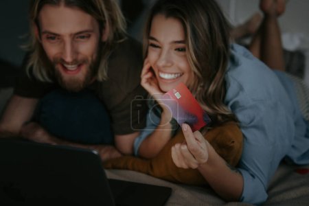 Téléchargez les photos : Heureux couple amoureux regardant ordinateur portable et en utilisant la carte de crédit tout en faisant des achats en ligne de la maison - en image libre de droit