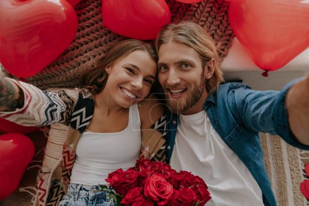 Téléchargez les photos : Vue de dessus du couple heureux amoureux tenant des fleurs et faisant selfie avec des ballons rouges en forme de coeur autour d'eux - en image libre de droit