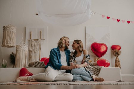 Téléchargez les photos : Couple amoureux romantique tenant la main et s'appuyant sur le lit avec des ballons rouges en forme de coeur sur le fond - en image libre de droit