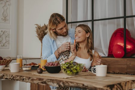 Photo for Young romantic couple enjoying healthy breakfast at home together with red heart shape balloons on background - Royalty Free Image