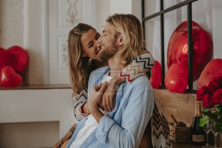 Foto de Joven pareja romántica abrazando y sonriendo mientras celebra el Día de San Valentín en la casa decorada - Imagen libre de derechos