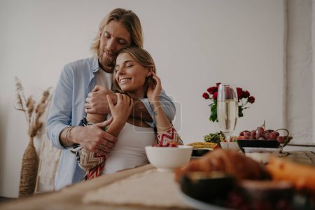 Foto de Joven pareja cariñosa abrazando y sonriendo mientras disfrutan de una cena romántica en casa juntos - Imagen libre de derechos