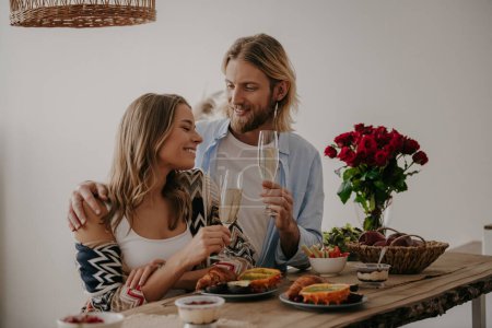 Foto de Romántico joven pareja cariñosa brindis con champán mientras se celebra aniversario en la mesa en casa - Imagen libre de derechos