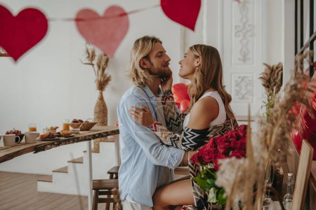 Foto de Pareja romántica joven abrazándose cara a cara mientras celebra el día de San Valentín en la casa decorada - Imagen libre de derechos