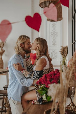 Foto de Joven pareja cariñosa abrazando y besándose mientras celebra el aniversario de amor en la casa decorada - Imagen libre de derechos