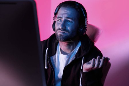 Photo for Depressed young man looking at the computer monitor and gesturing while sitting against colorful background - Royalty Free Image