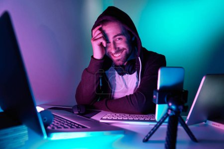 Photo for Handsome young man looking at camera and smiling during live stream against colorful background - Royalty Free Image