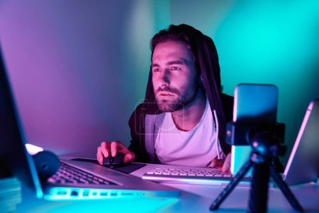 Téléchargez les photos : Confiant jeune homme en utilisant l'ordinateur pendant le flux en direct sur fond coloré - en image libre de droit