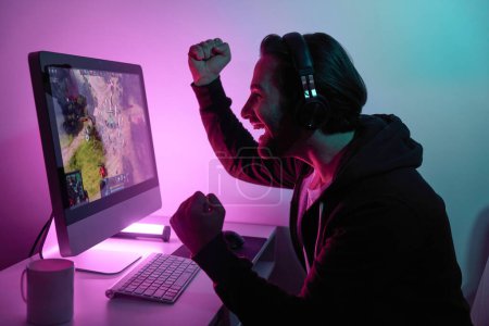 Foto de Vista lateral del hombre feliz haciendo gestos mientras juega juego de ordenador contra fondo colorido - Imagen libre de derechos