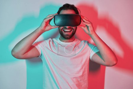 Photo for Happy young man adjusting his virtual reality eyeglasses with colorful shadows in the background - Royalty Free Image