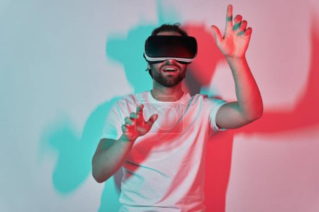 Foto de Joven excitado en gafas de realidad virtual gestos con sombras de colores en el fondo - Imagen libre de derechos