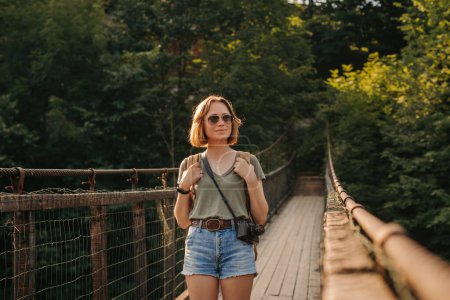 Foto de Atractiva joven viajera con mochila caminando por el puente escénico - Imagen libre de derechos