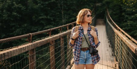 Téléchargez les photos : Belle jeune voyageuse avec sac à dos marchant par le pont pittoresque - en image libre de droit