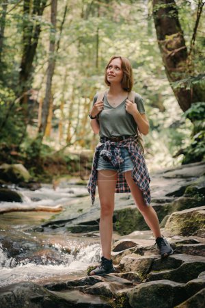 Foto de Hermosa joven viajera con mochila caminando por las piedras a lo largo del río de montaña - Imagen libre de derechos