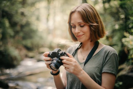Téléchargez les photos : Belle jeune voyageuse utilisant un appareil photo tout en photographiant la vue panoramique sur la rivière de montagne - en image libre de droit