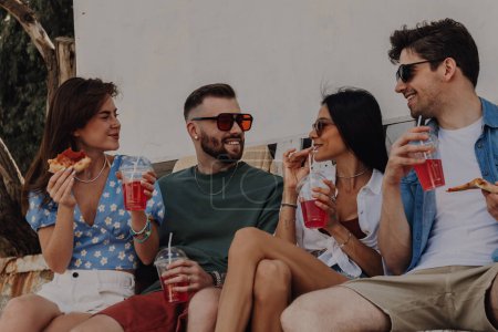 Foto de Grupo de amigos alegres disfrutando de comida y bebidas mientras pasan tiempo al aire libre juntos - Imagen libre de derechos
