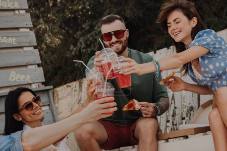 Foto de Grupo de amigos brindando con cócteles mientras disfrutan de pizza al aire libre juntos - Imagen libre de derechos