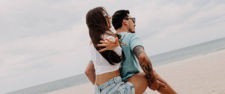 Téléchargez les photos : Beau jeune homme piggyback son copine tout en s'amusant sur la plage ensemble - en image libre de droit