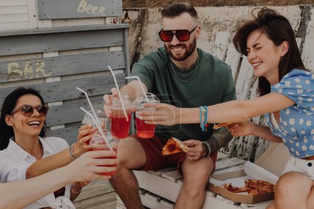 Foto de Felices jóvenes amigos brindando con cócteles mientras disfrutan de la pizza al aire libre juntos - Imagen libre de derechos