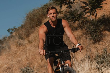 Foto de Hombre atlético joven en ropa deportiva montar en bicicleta por montaña colina al aire libre - Imagen libre de derechos