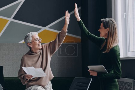 Photo for Two confident women giving high five and smiling while working in the office together - Royalty Free Image