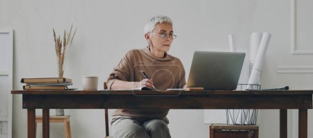 Foto de Empresa senior concentrada que usa laptop mientras está sentada en su lugar de trabajo - Imagen libre de derechos