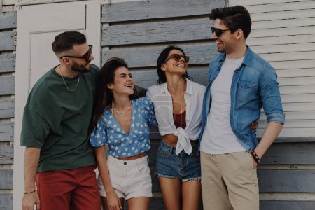 Téléchargez les photos : Groupe d'amis joyeux parlant et souriant tout en passant la journée d'été à l'extérieur ensemble - en image libre de droit