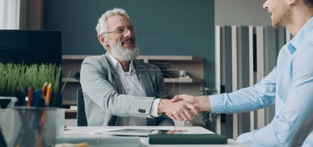 Photo for Two happy businessmen shaking hands while sitting in the office together - Royalty Free Image