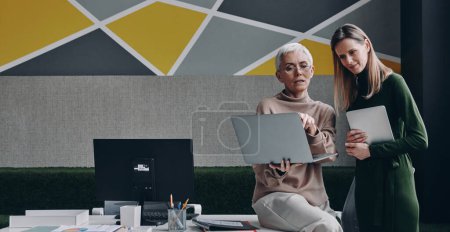 Foto de Dos mujeres seguras que usan tecnologías y se comunican mientras trabajan juntas en la oficina - Imagen libre de derechos