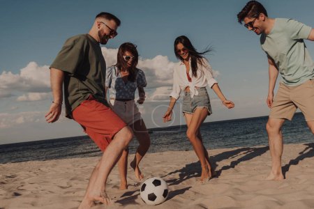 Téléchargez les photos : Groupe de jeunes gens jouant au football et s'amusant sur la plage ensemble - en image libre de droit
