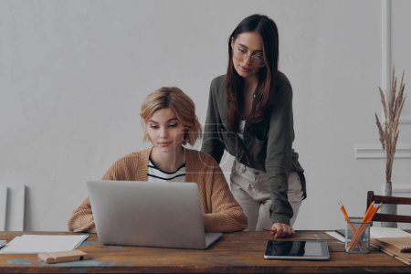 Téléchargez les photos : Deux jeunes femmes confiantes regardant un ordinateur portable tout en travaillant ensemble au bureau de création - en image libre de droit