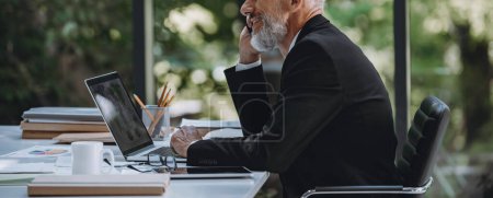 Foto de Confiado hombre de negocios maduro hablando en el teléfono móvil mientras estaba sentado en su lugar de trabajo en la oficina - Imagen libre de derechos