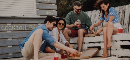 Téléchargez les photos : Groupe d'amis heureux profitant de la nourriture et des boissons tout en se relaxant près de la plage café ensemble - en image libre de droit