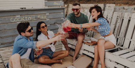 Foto de Grupo de amigos felices brindando con cócteles mientras disfrutan de pizza al aire libre juntos - Imagen libre de derechos