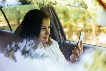 Téléchargez les photos : Pose prise par la fenêtre de la voiture d'une jeune femme souriant et prenant selfies tandis que la voiture est arrêtée - en image libre de droit